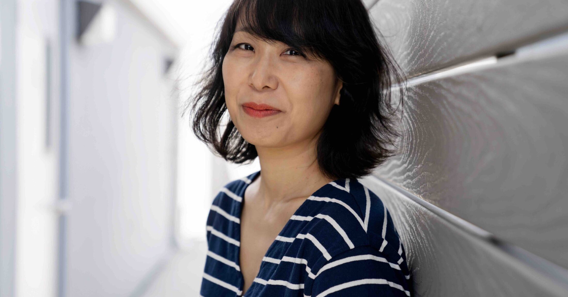 Photograph of E. Tammy Kim. She wears a striped shirt and smiles at the camera.