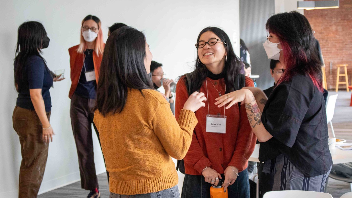 A photograph of graduate students at the Spring 2025 A/P/A Graduate Student Symposium. They standing in groups talking and smiling.