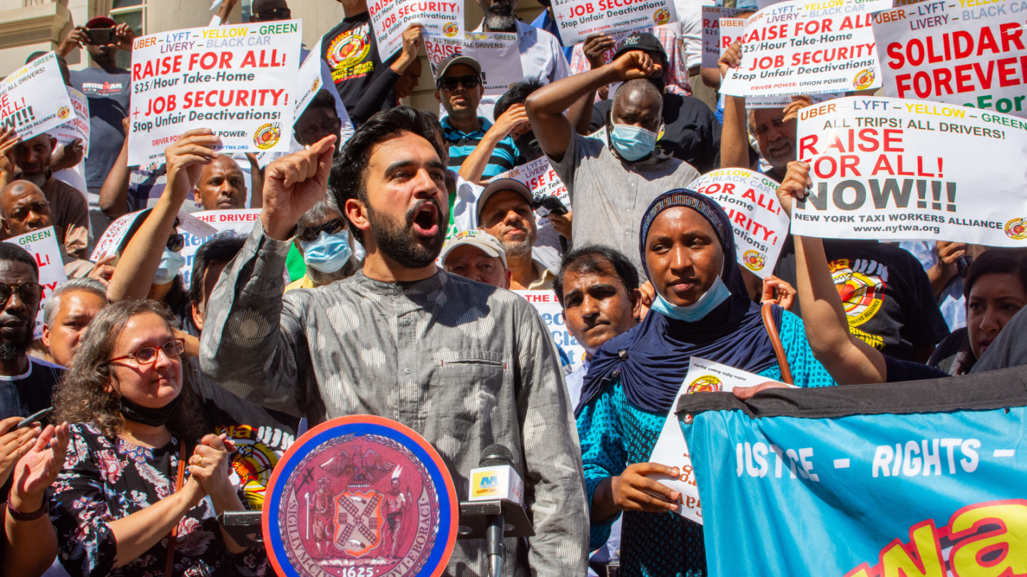 A photograph of Zohran Mamdani speaking at a NYTWA Rally in 2022.