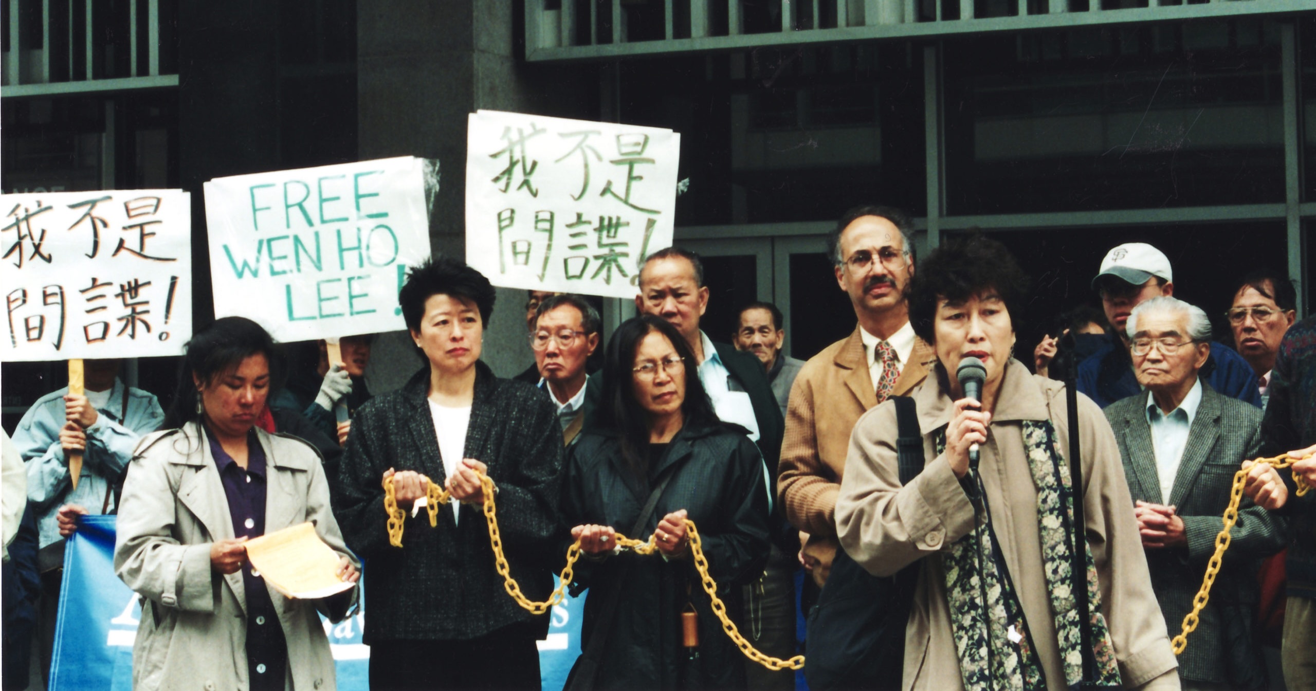 Activist from Chinese for Affirmative Action stand in a line, holding signs and a yellow chain to protest Weh Ho Lee's nine months of solitary confinement.