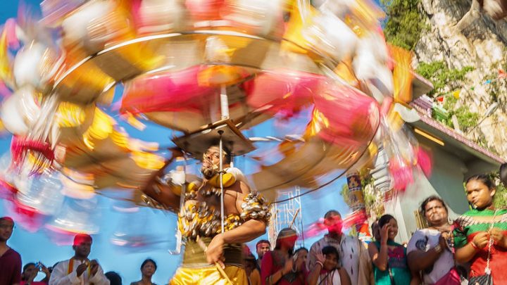 A photograph of a Kavadi. It spins in the air above a crowd.