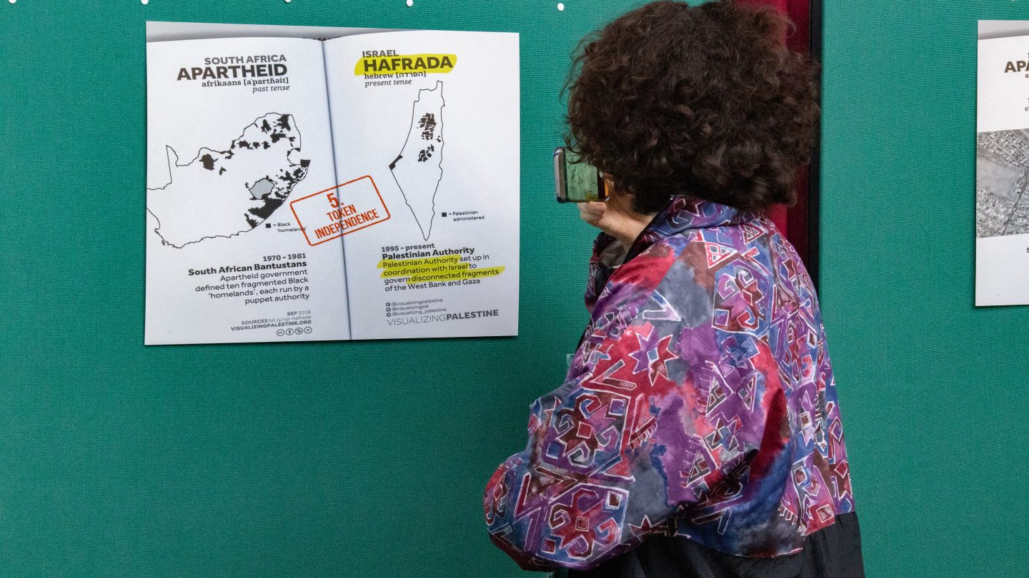 A photograph of a visitor to a Visualizing Palestine exhibition viewing one of the infographics the organization created.