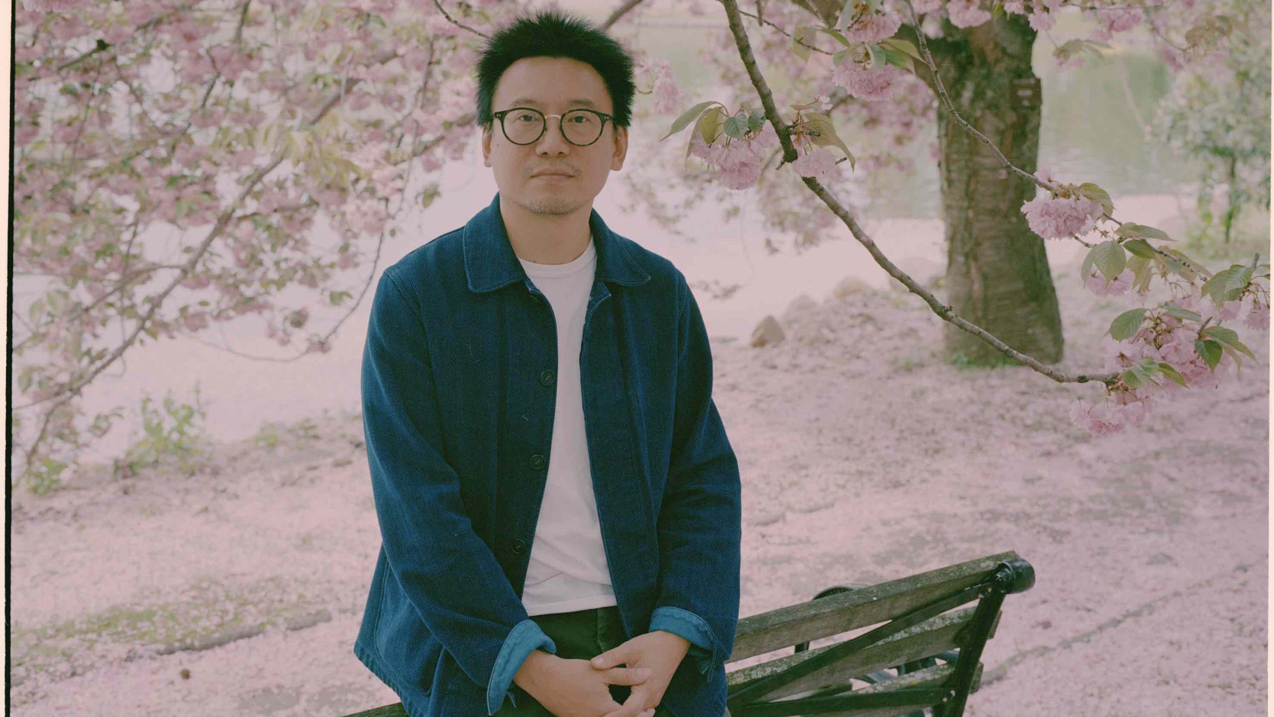 A photograph of Hua Hsu leaning against a park bench